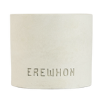 A handcrafted Erewhon candle made of concrete, with a white finish and the brand name embossed on the front.