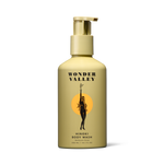 A sleek aluminum bottle with a pump dispenser, labeled 'Wonder Valley Hinoki Body Wash', featuring a design of a figure in a circle and a sun motif.