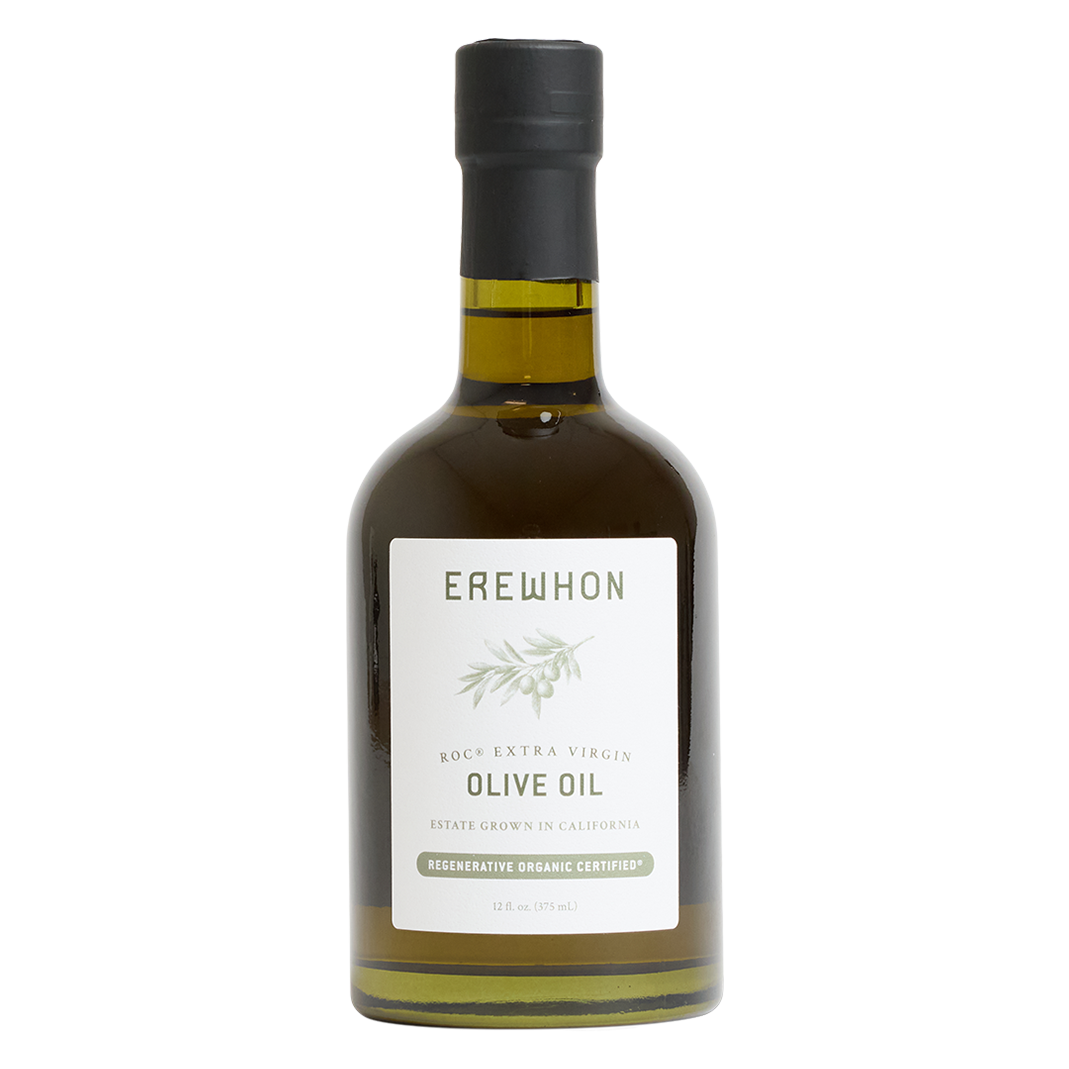 A bottle of Erewhon Roasted Extra Virgin Olive Oil on a solid white background. The bottle is made of dark glass showing the golden-olive oil inside, has a black screw cap, and a white label with green text and a small olive branch illustration.